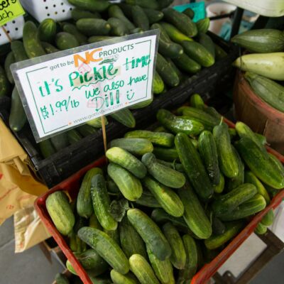 Close-up of fresh cucumbers and squash for sale at a North Carolina farmers market stall.