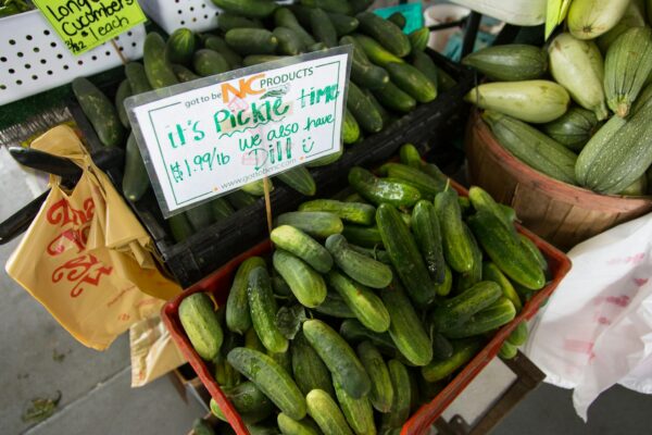 Close-up of fresh cucumbers and squash for sale at a North Carolina farmers market stall.