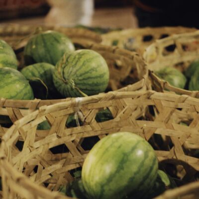 Green watermelons displayed in rustic woven baskets at a bustling market.