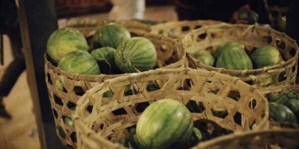 Green watermelons displayed in rustic woven baskets at a bustling market.