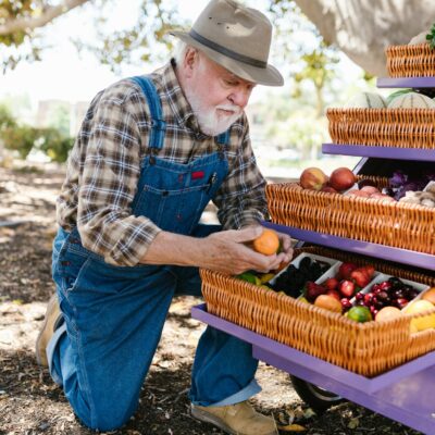 Senior farmer arranging fresh produce baskets at an outdoor market stall on a sunny day.