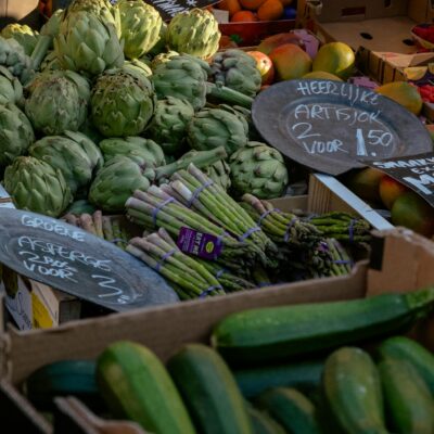 Vibrant display of fresh organic vegetables at an outdoor farmers market showcasing artichokes, zucchini, and asparagus.